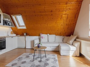 A cozy loft bedroom with a sloped ceiling, a white sofa, a small round table, and a kitchen area with white cabinets and appliances. - Apartment Emi by Interhome (Badacsonytomaj)