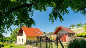 Uma casa de dois andares com telhado vermelho, varanda e quintal cercado.