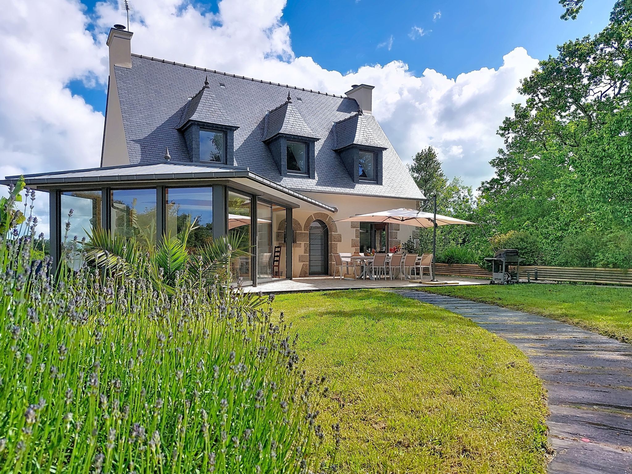 A modern house with a covered patio, a stone facade, and a large lawn.