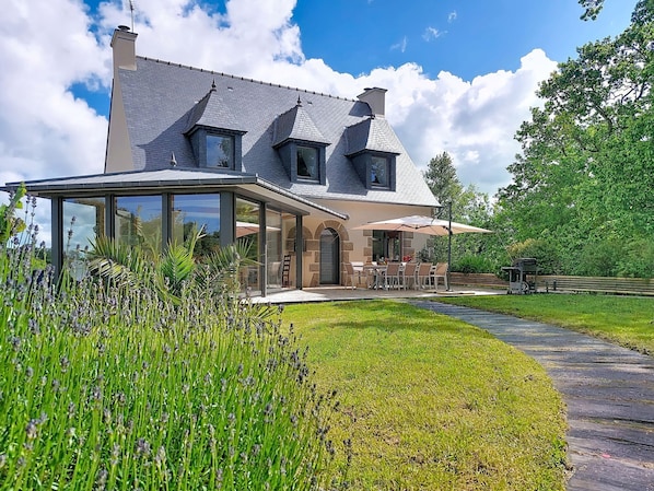 A modern house with a covered patio, a stone facade, and a large lawn.