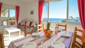 A dining area with a table set for four, a sofa, and a view of the sea. - La Rocade by Interhome (Théoule sur mer)