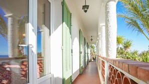 A corridor with green shutters, white walls, and a tiled floor leading to a balcony with a view of the sea. - La Rocade by Interhome (Théoule sur mer)