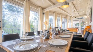 A dining area with a long wooden table set for six, large windows, and a view of trees outside. - Le Murier by Interhome (Fréjus)