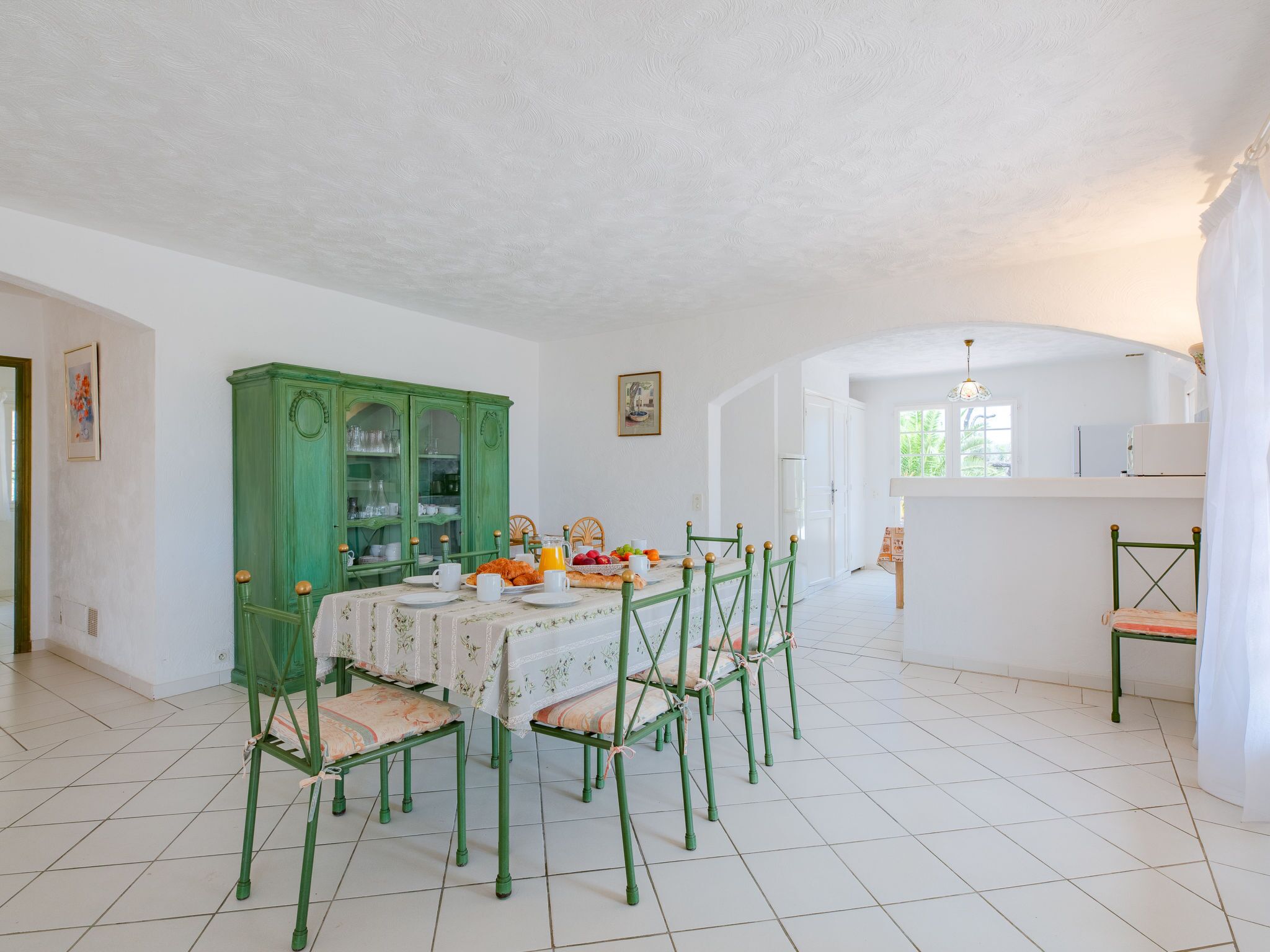 Un coin repas avec un meuble vert, un sol carrelé de blanc et une table mise pour le petit-déjeuner.