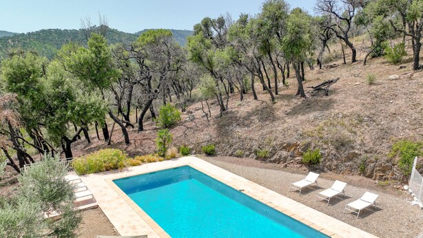 A rectangular pool with a tiled border, surrounded by a gravel area with white lounge chairs and a single umbrella. - Mas des Chênes by Interhome (Grimaud)