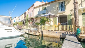 A canal-side building with a wooden dock, a boat docked nearby, and a clear blue sky. - Bleu Azur by Interhome (Port Grimaud)