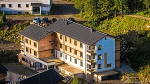 Monikerroksinen rakennus, jossa on moderni arkkitehtoninen ilme. Siinä on yhdistelty puuta ja vaaleita ulkoseiniä, ja katto on tasainen.