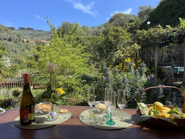 A table set outdoors with a bottle, glasses, and a basket of lemons.