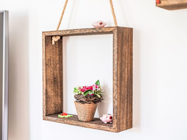 A rustic wooden frame with a woven basket containing pink flowers and green leaves, hanging on a wall.