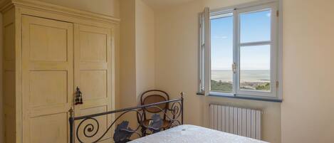 A bedroom with a bed, a window with a view, a wardrobe, and a chair.