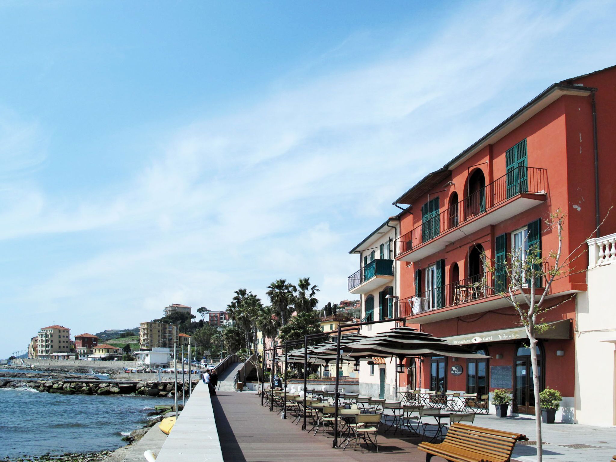 A coastal promenade with outdoor seating, a café, and a view of the sea.