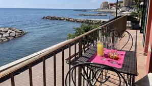 Un balcon avec une table dressée pour deux personnes, offrant une vue sur une côte rocheuse et la mer.