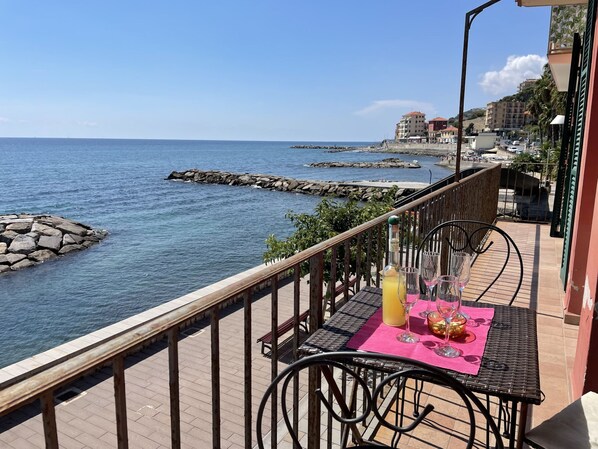 A balcony with a table set for two, overlooking a rocky coastline and the sea.