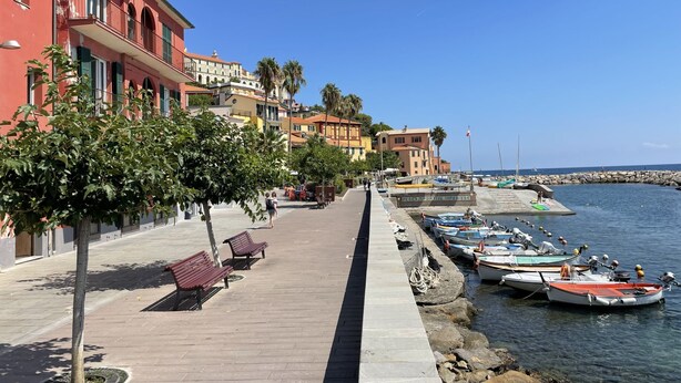 Une promenade en bord de mer bordée de bâtiments aux couleurs vives, un sentier pavé agrémenté de bancs et des bateaux amarrés au quai.