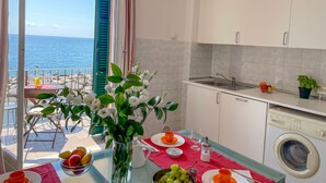 Une cuisine avec vue sur la mer, un coin repas avec une table dressée pour deux personnes, et un lave-linge.