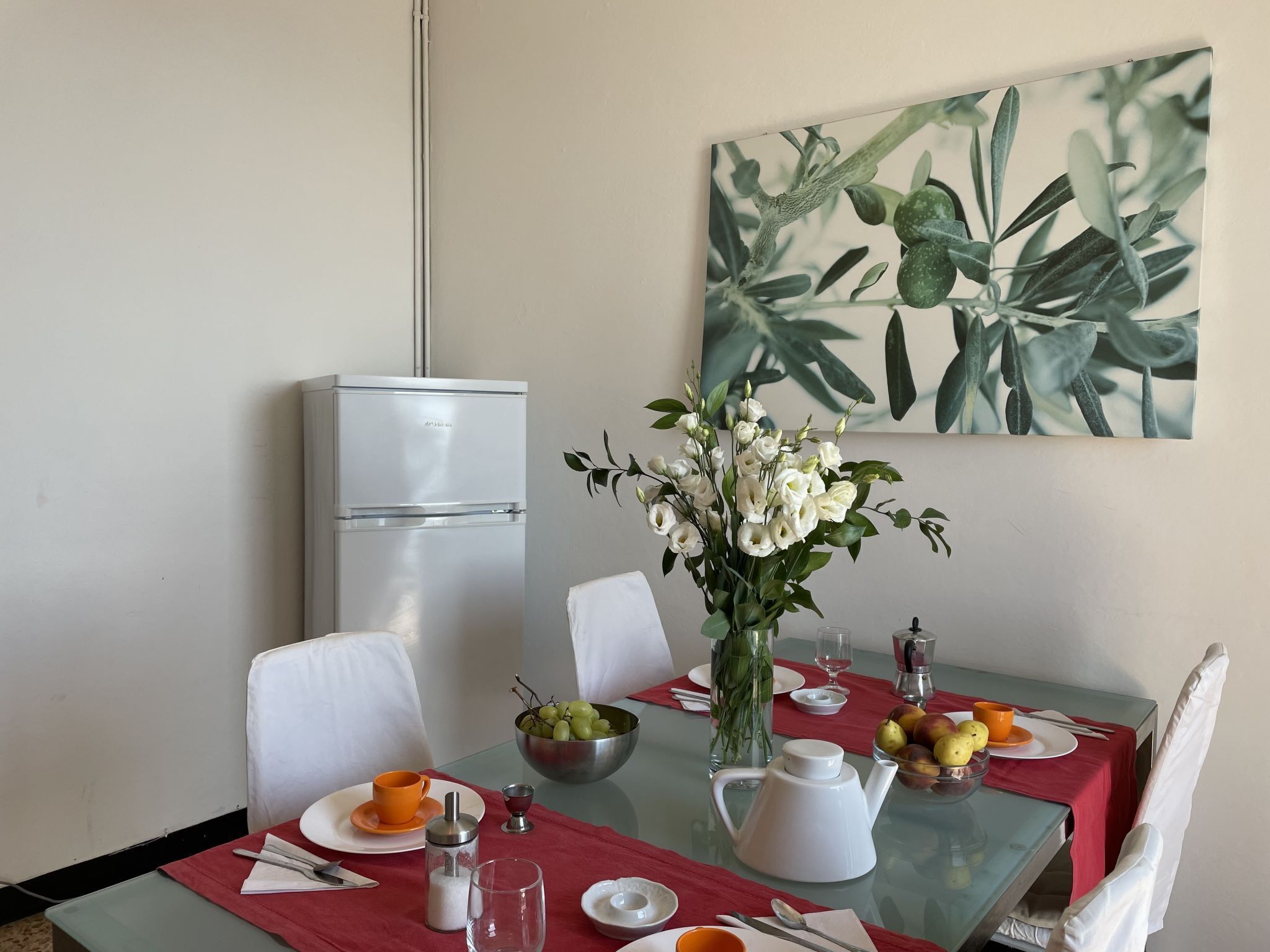 Un coin repas avec une table dressée pour deux personnes, un réfrigérateur blanc et un tableau accroché au mur.