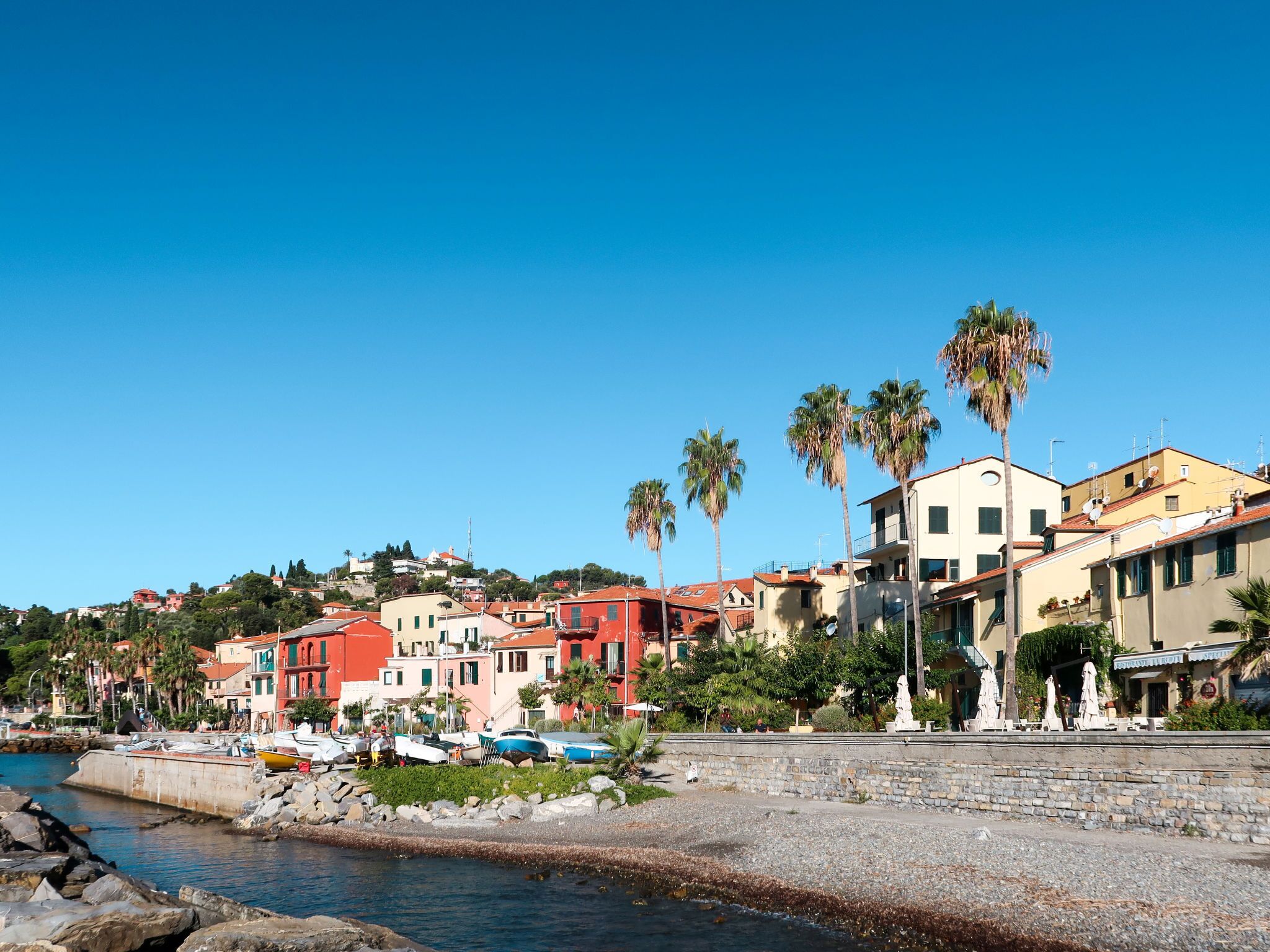 A coastal town with colorful buildings, a rocky shoreline, and palm trees.
