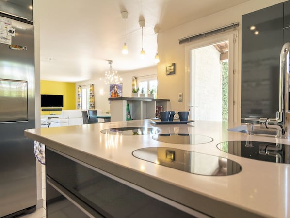 A modern kitchen with a stainless steel refrigerator, a central island with a sink, and a dining area with a sofa and chairs.