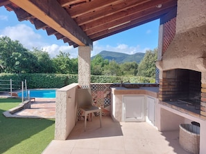 An outdoor patio with a pool, a grill, and a view of mountains.