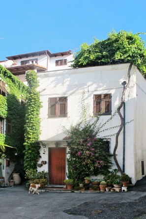Un edificio bianco con persiane in legno, una porta di legno e piante in vaso di fronte.