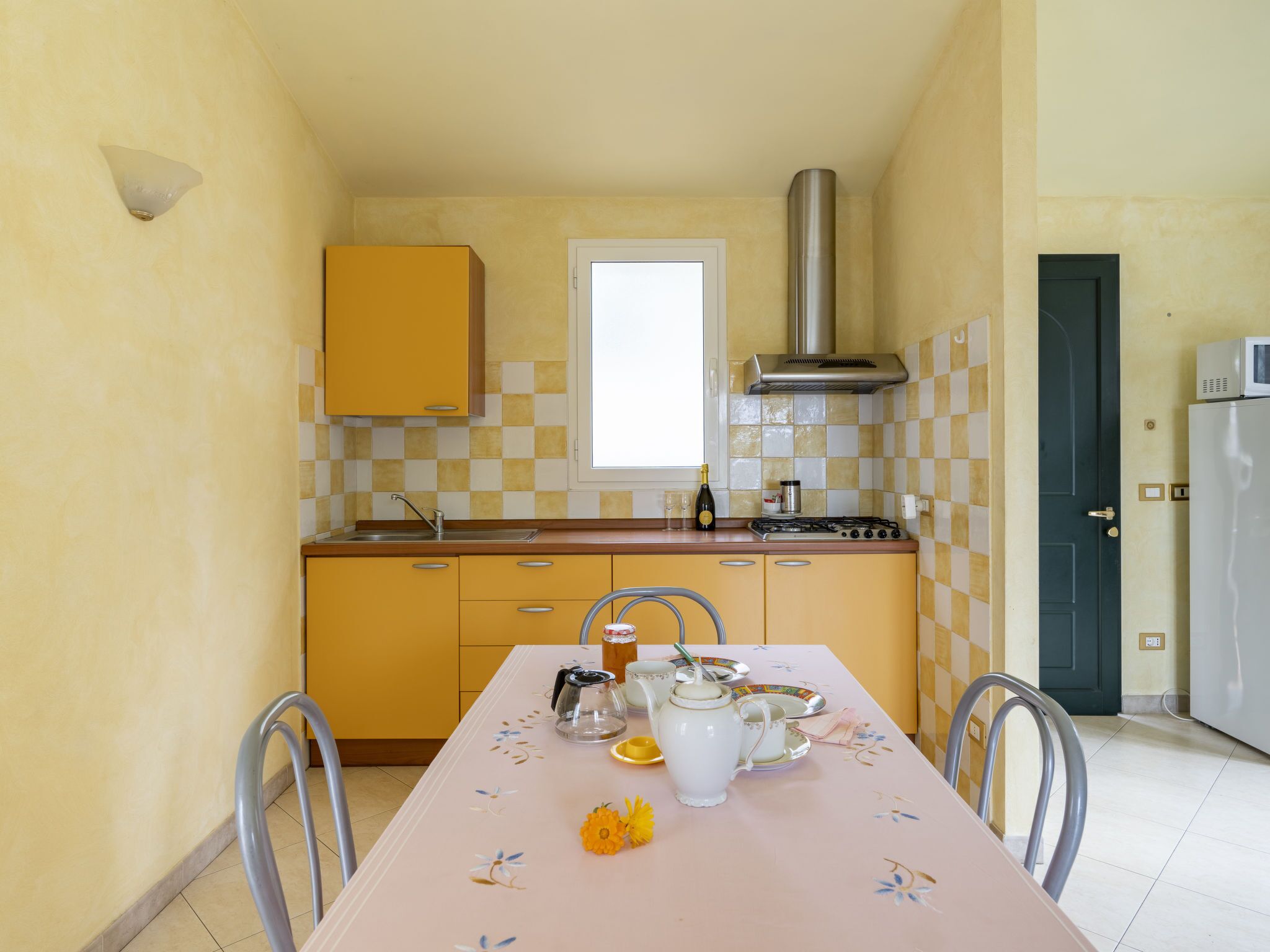 A compact kitchen with yellow cabinets, a stainless steel range hood, a microwave, and a sink.