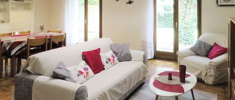 A living room with a sofa, armchairs, a dining table, and a kitchen area.