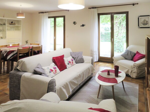 A living room with a sofa, armchairs, a dining table, and a kitchen area.