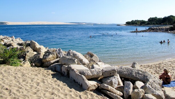 Una playa con agua azul cristalina, formaciones rocosas y una orilla arenosa.