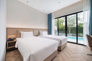 Habitació d'hotel amb dos llits, un escriptori i vista a una piscina.