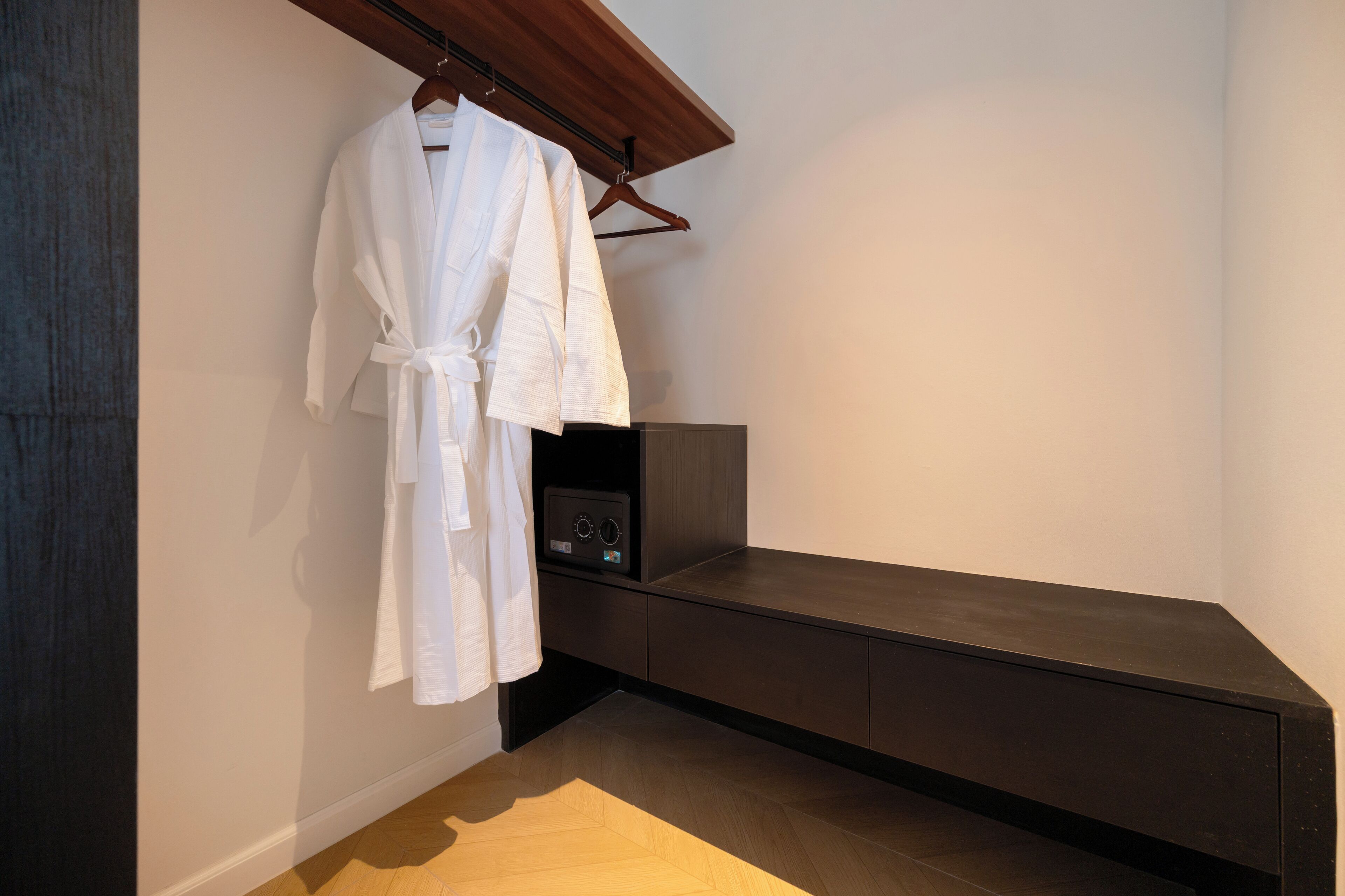 A modern bathroom with a dark bench, a white robe hanging on a rack, and a small black appliance on the bench.