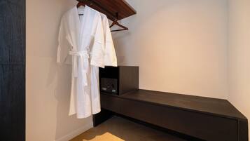 A modern bathroom with a dark bench, a white robe hanging on a rack, and a small black appliance on the bench.