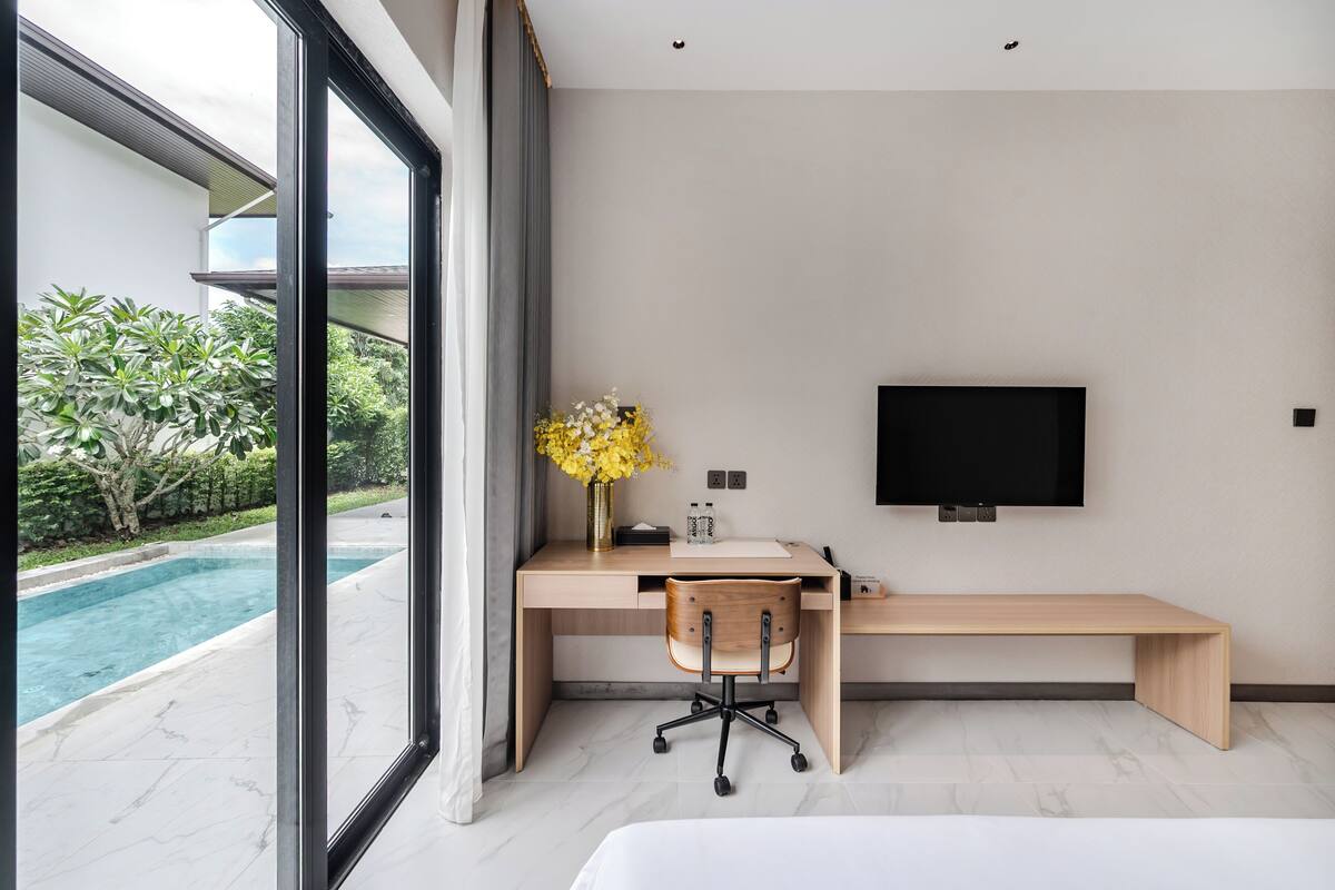 Un dormitorio moderno con un ventanal grande, un escritorio, una silla, una cama y un televisor.