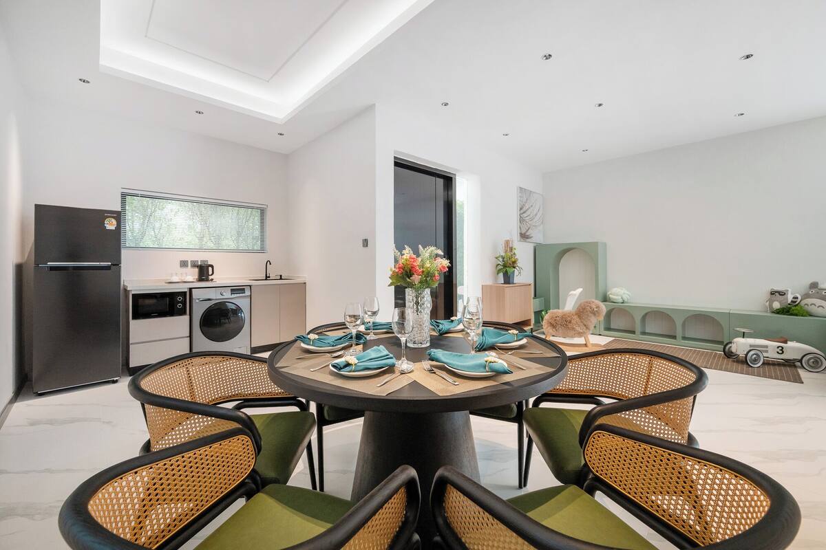 Un comedor moderno con una mesa redonda, sillas verdes y una cocina al fondo.