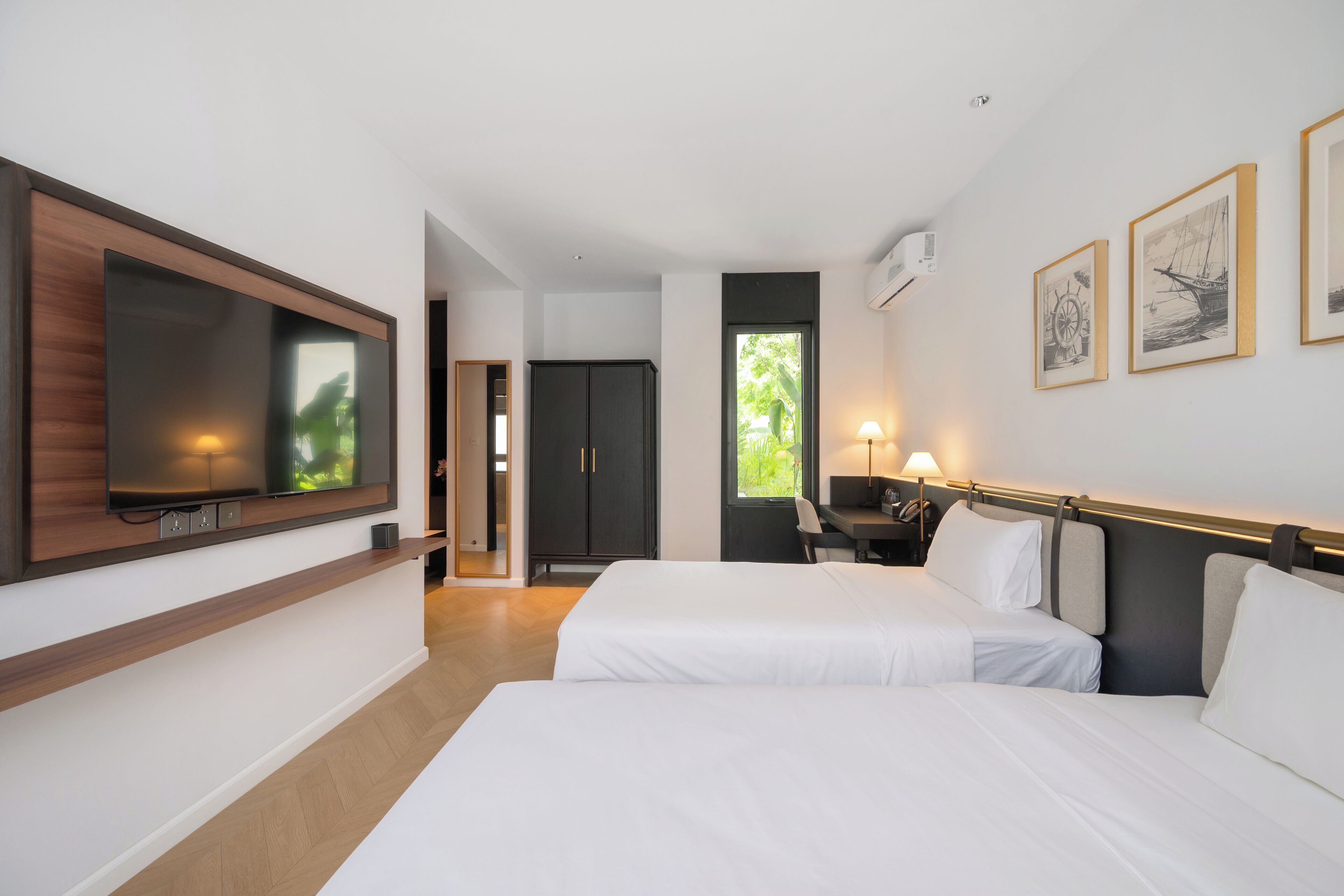 A hotel room with two beds, a TV mounted on the wall, a desk with a chair, and artwork on the wall.