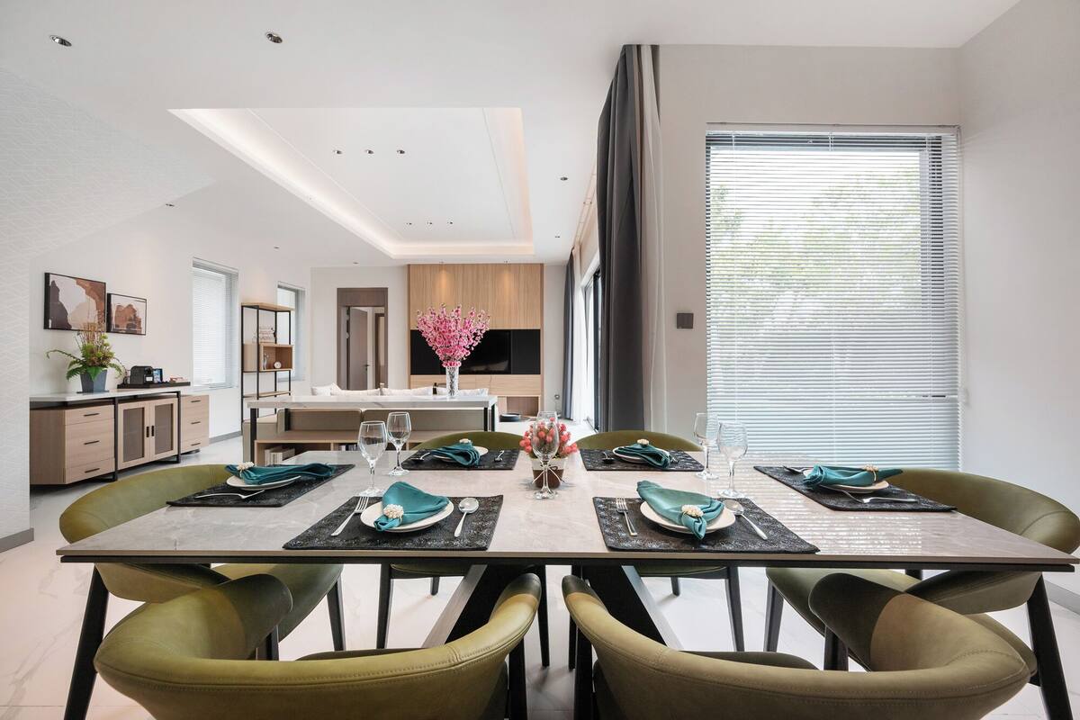 Un comedor moderno con una mesa rectangular dispuesta para cuatro personas, rodeada de sillas tapizadas en verde.
