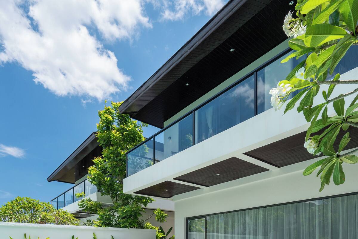 Una casa moderna con piscina, dos sillones de descanso y un amplio ventanal de vidrio.