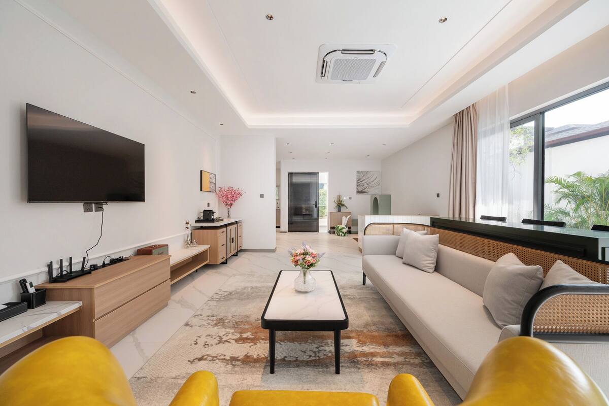 Una sala de estar moderna con un televisor de pantalla plana, un sofá, una mesa de centro y un comedor con un aparador de madera y una pequeña mesa.