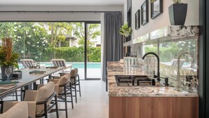 Una cocina moderna con una isla grande, un comedor con sillas y vistas a una piscina.