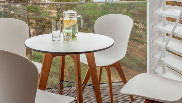 Un balcon avec une table, des chaises et une carafe d’eau contenant une tranche de citron.