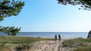 Un sentier sablonneux qui mène à une plage où l’on voit deux personnes se promener.