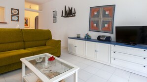 A living room with a green sofa, a glass coffee table, white cabinets, a flat-screen TV, and decorative wall art. - Golf Royal Delta by Interhome (Pals)