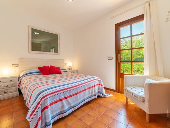 A bedroom with a bed, a nightstand, a chair, a window, and a door. - Ca Na Rosa by Interhome (Llombards/C.Llombards/C.S'Almonia)