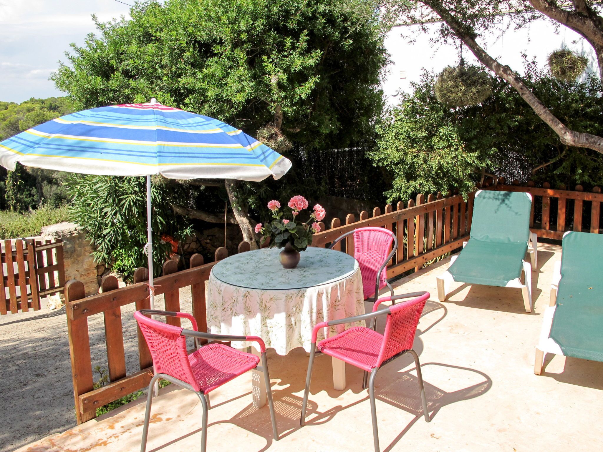 Un espace extérieur aménagé avec une table ronde, deux chaises roses et un parasol à rayures.