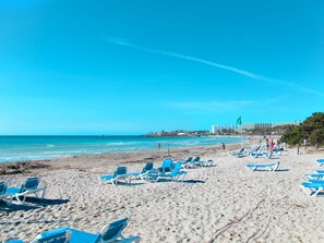 A beach with rows of blue lounge chairs and a hotel in the background.