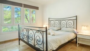Una camera da letto con un letto a struttura in metallo, un comodino, una lampada e una finestra vista alberi.