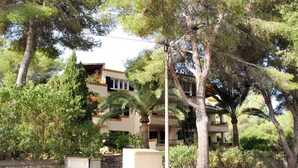 Un edificio a più piani con balconi, immerso nel verde e circondato da un muro in pietra.