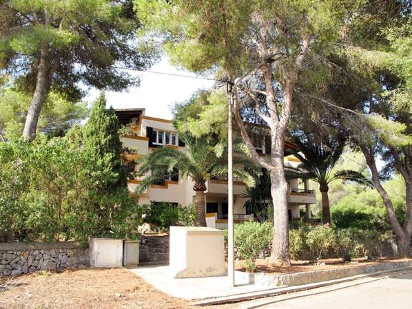 A multi-story building with balconies, surrounded by trees and a stone wall. - Los Pinos by Interhome (Cala Murada)