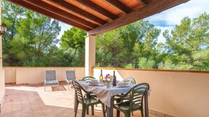 Una terrazza esterna con tavolo apparecchiato per mangiare, circondata da sedie e un pergolato sopra.
