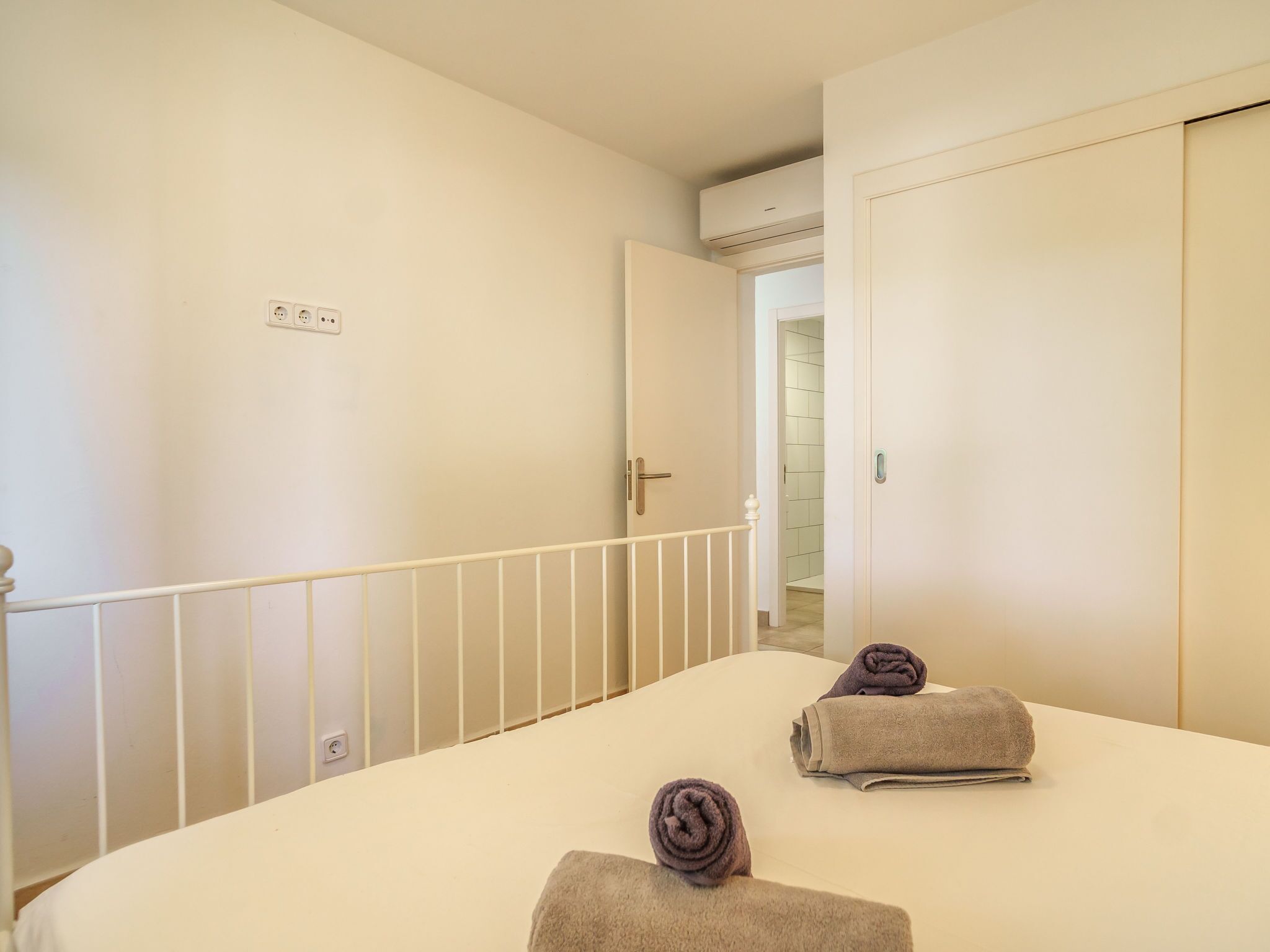Una habitación de hotel con una cama, dos toallas, un pasamanos blanco y una puerta que da a un baño.