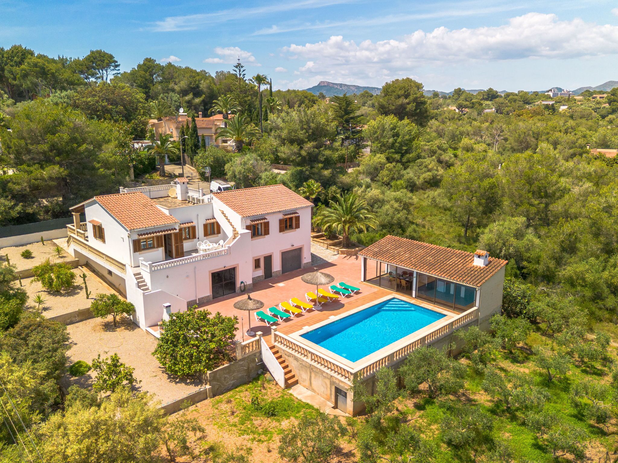 A large house with a swimming pool, surrounded by trees and hills.